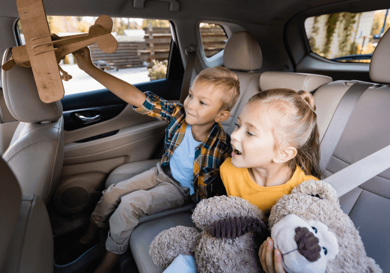 To børn på bagsædet i en bil. De leger med en flyvemaskine og en bamse