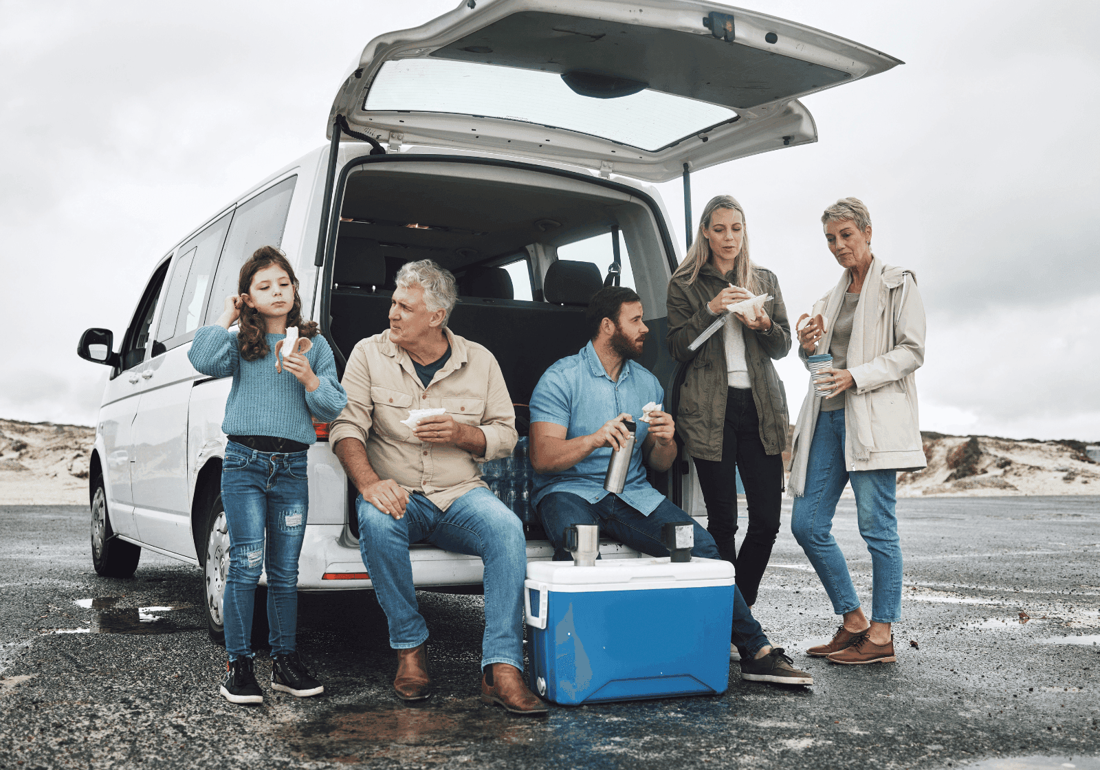 Familie står foran bagklap på bil og spiser mad fra køleboks