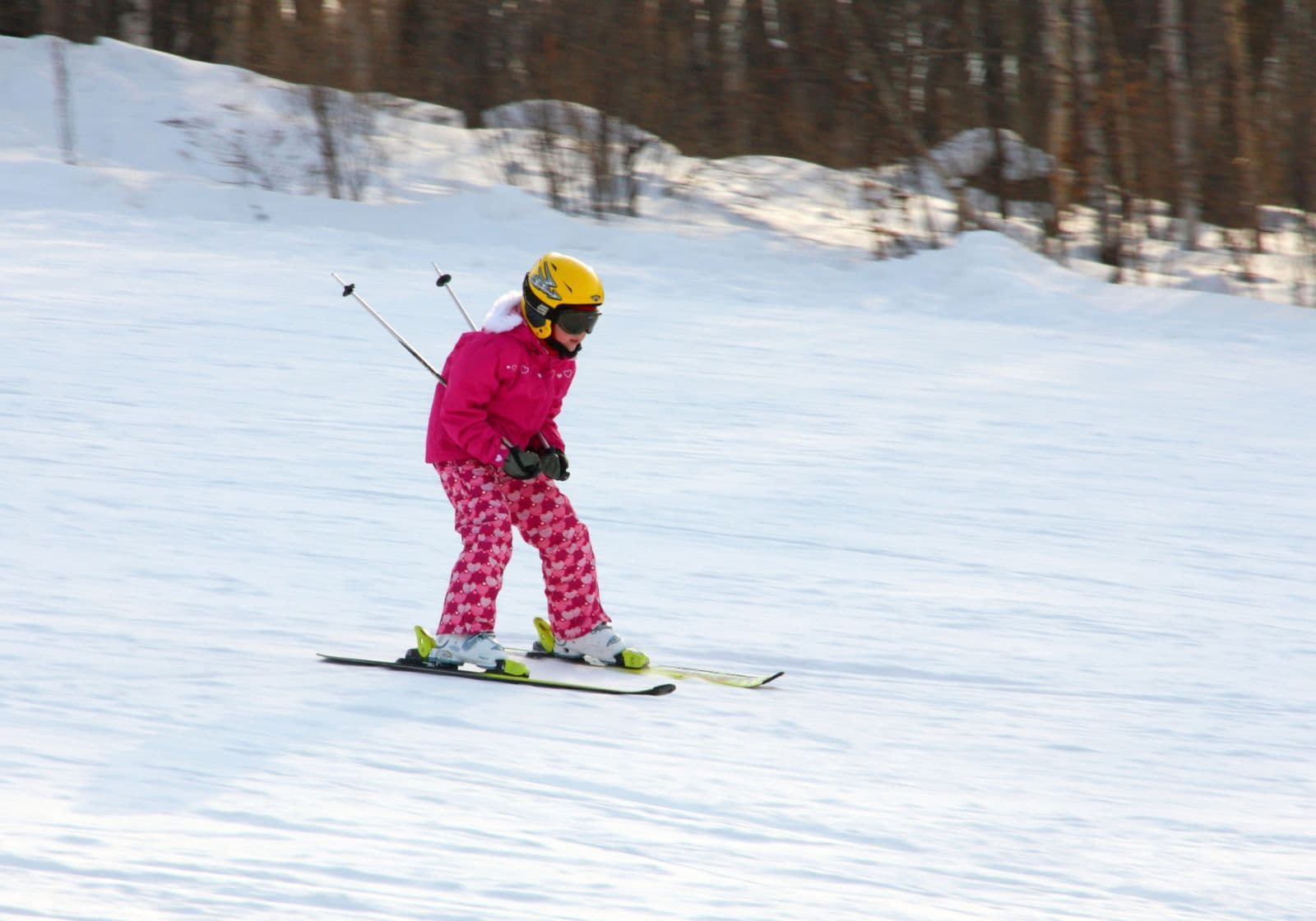 Lille pige, der står på ski ned ad bakke i vinterudstyr