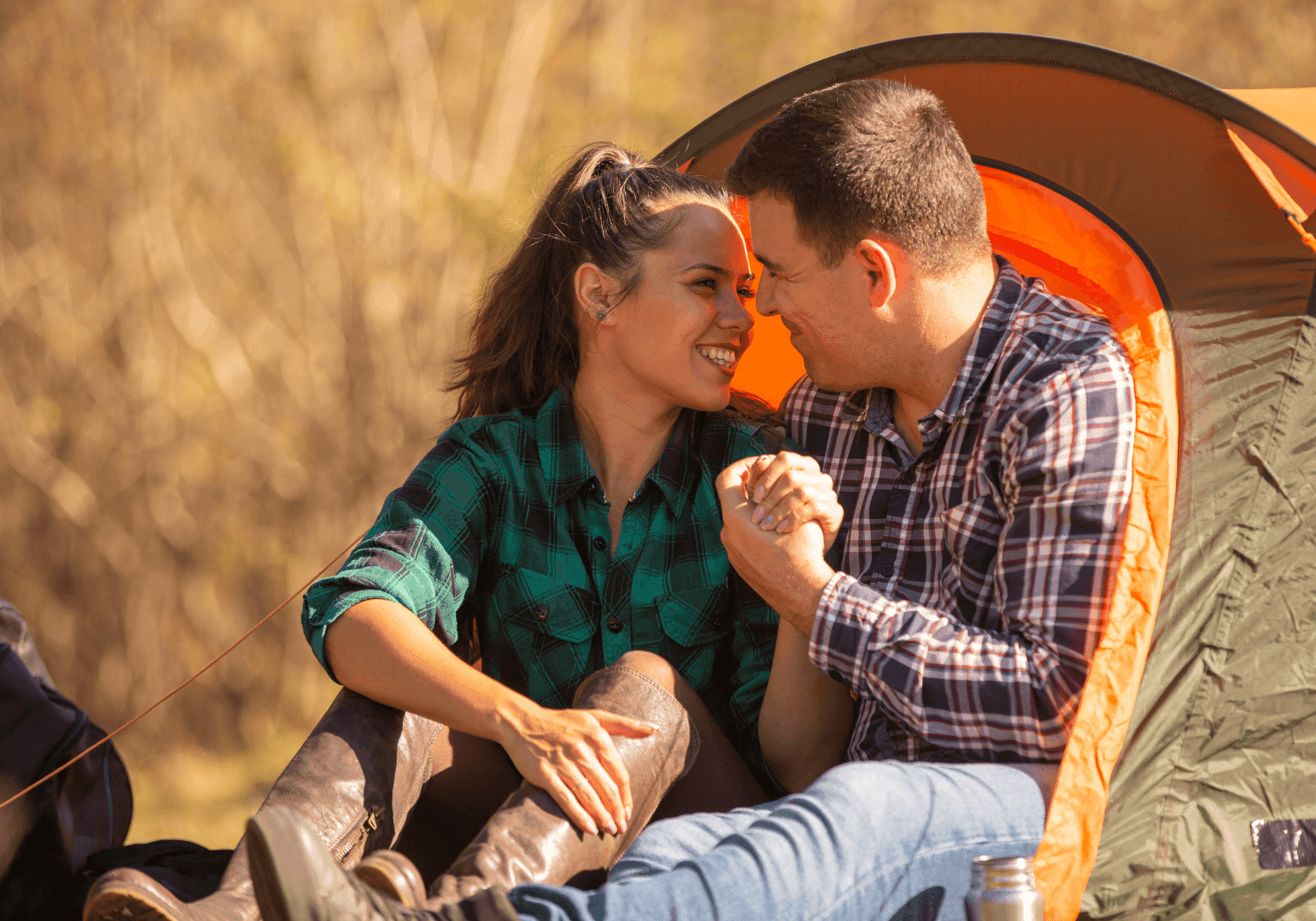 Et kærestepar smilende foran telt på campignplads. Romantisk atmosfære