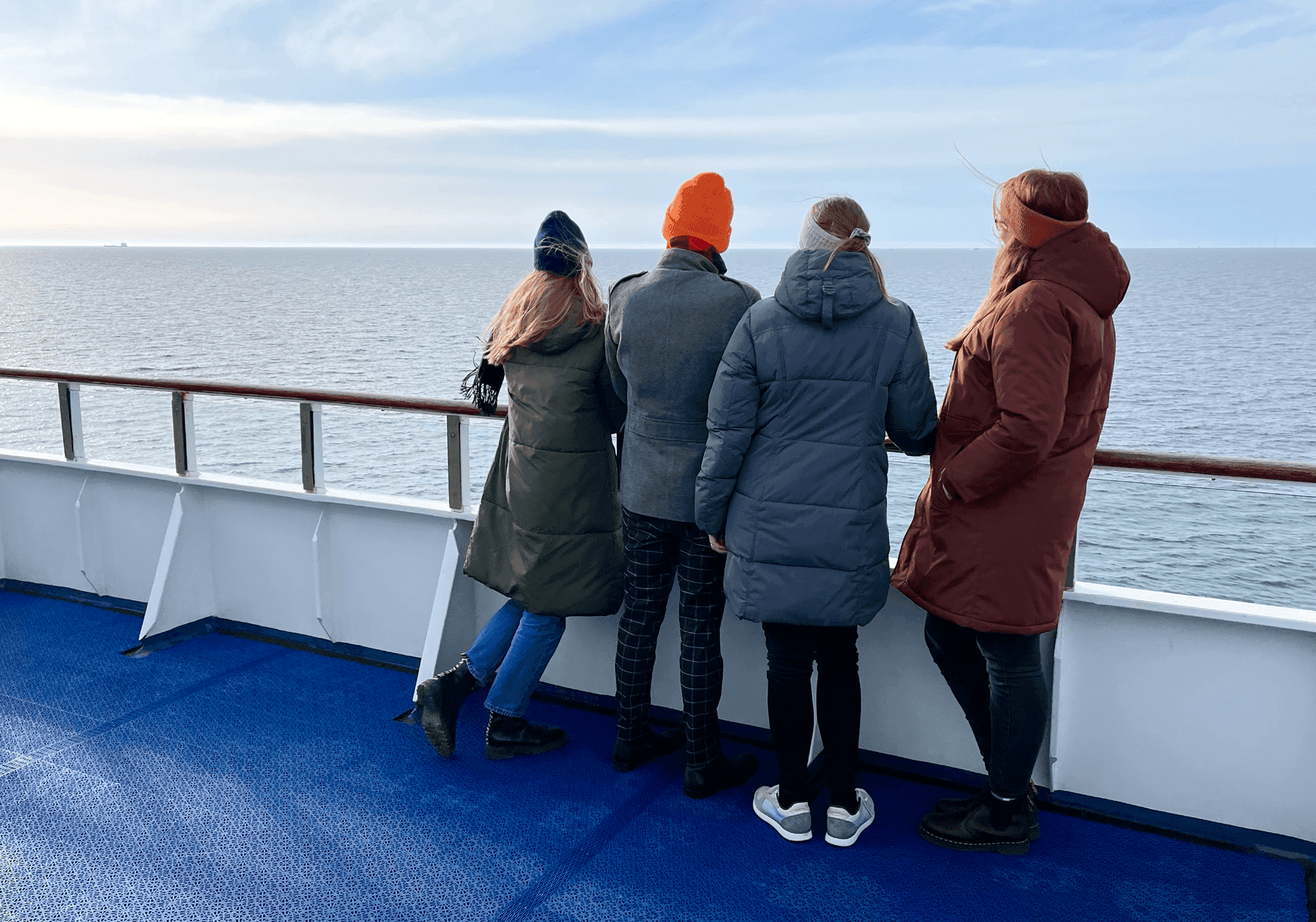 Fire personer i vintertøj står på færgen og kigger ud over havet